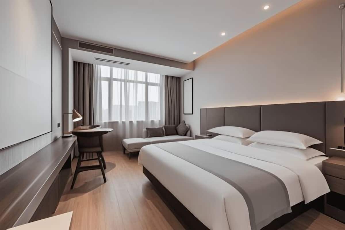 Una habitación de hotel moderna con una cama grande, un escritorio, un sofá y una ventana con cortinas.