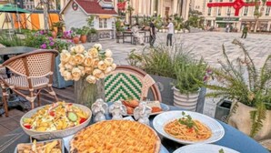 A dining table with various dishes including pizza, pasta, and fries, set outdoors with potted plants and a view of a street. - WGSY Hotel (Hefei Economic Development Zone Mingzhu Square University Town) (Hefei)