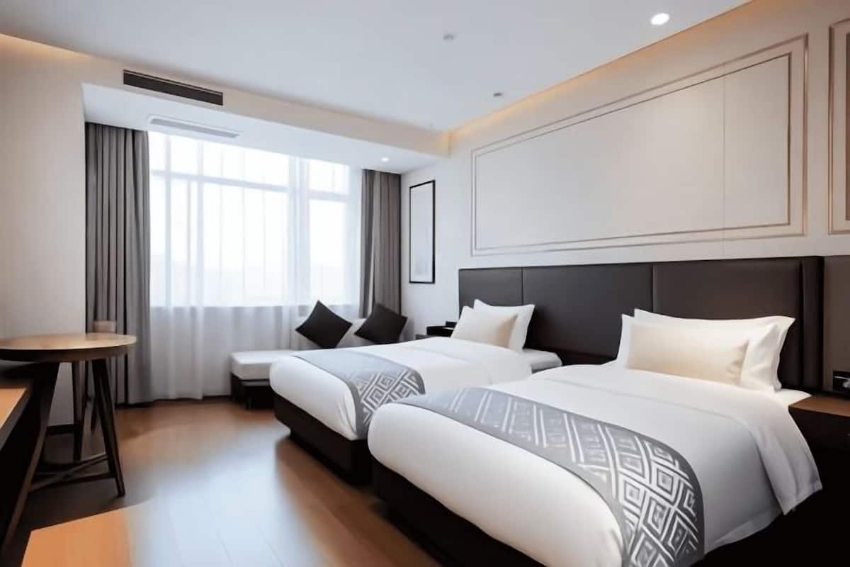 Habitación de hotel con dos camas, una mesita y un ventanal con cortinas.