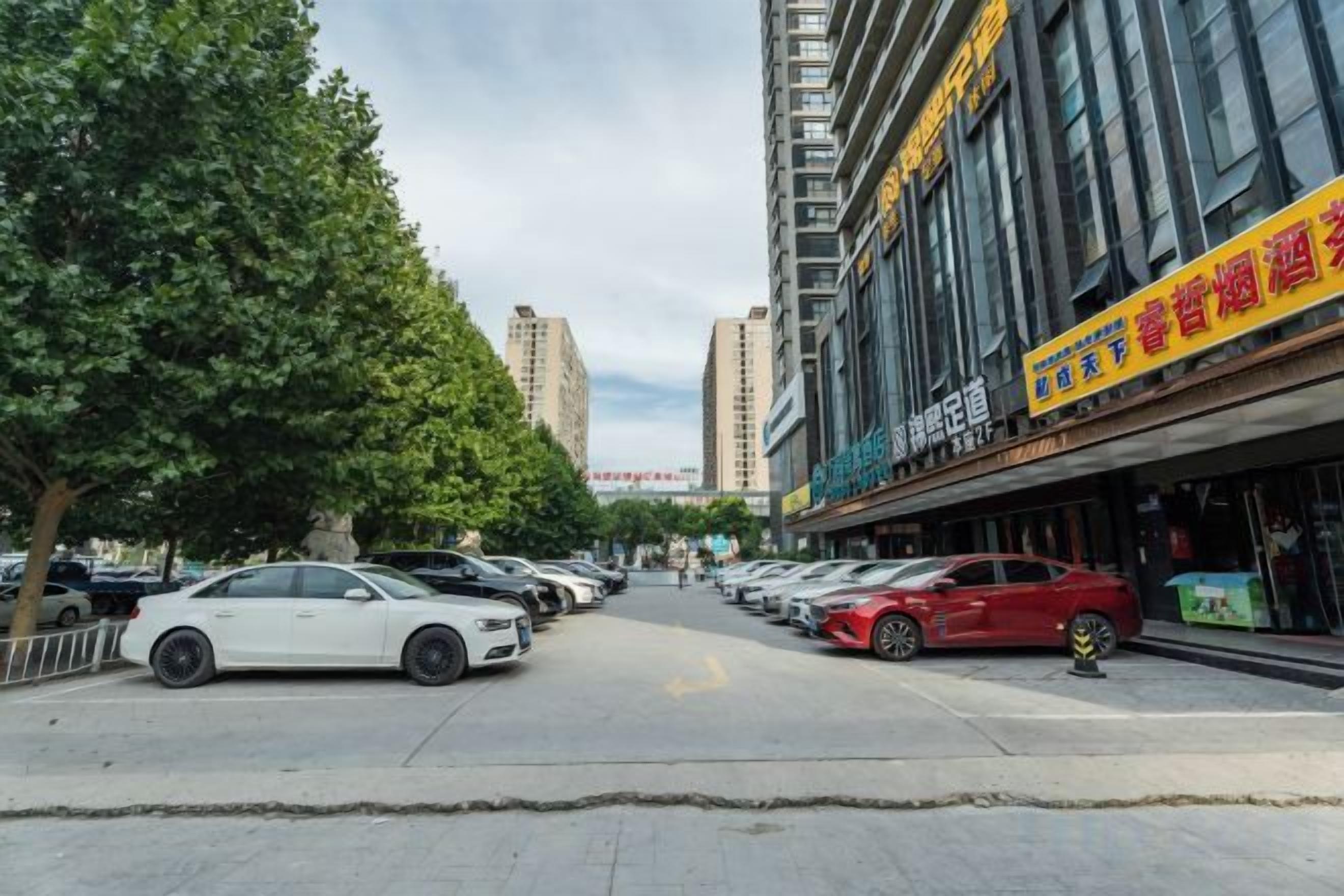 Una calle con coches estacionados, un edificio con un letrero y árboles.