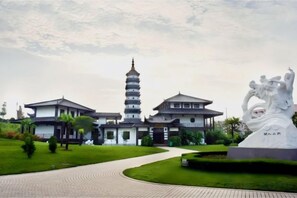 Um edifício tradicional com uma torre em estilo pagoda, uma estátua e um caminho pavimentado.