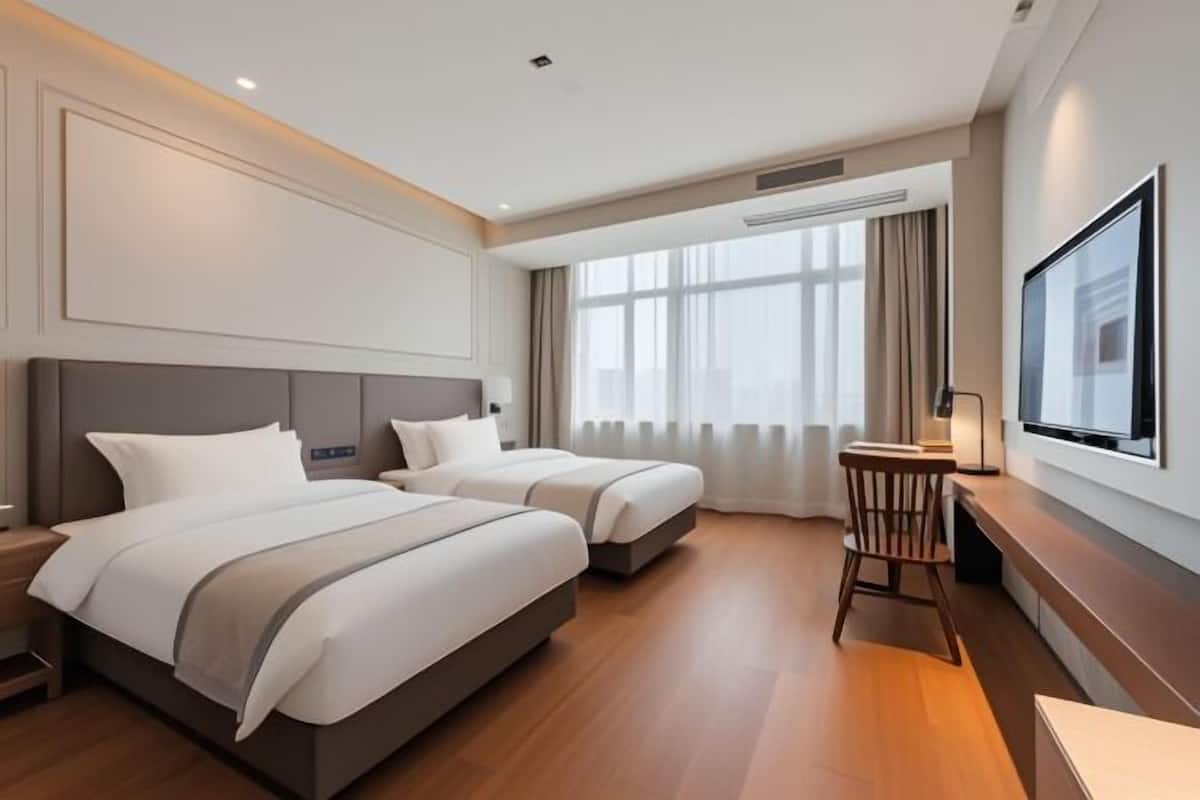 Una habitación de hotel con dos camas, un escritorio, una silla y un televisor en la pared.