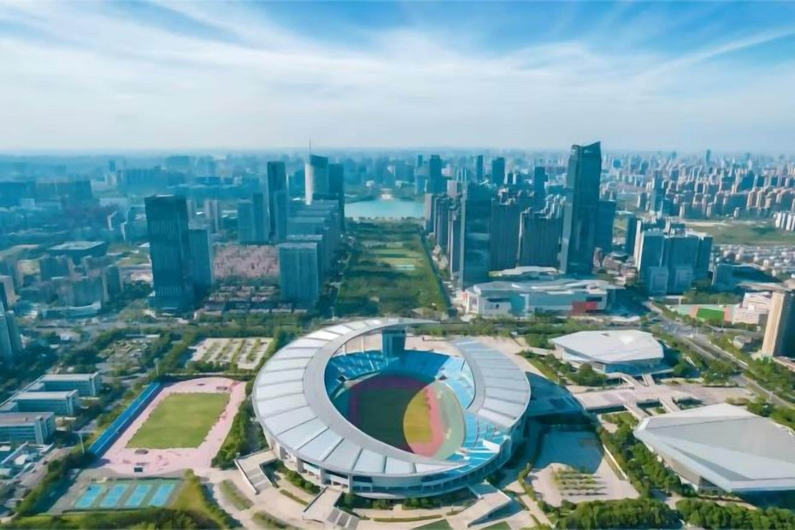 A stadium with a circular design surrounded by modern buildings and a river.