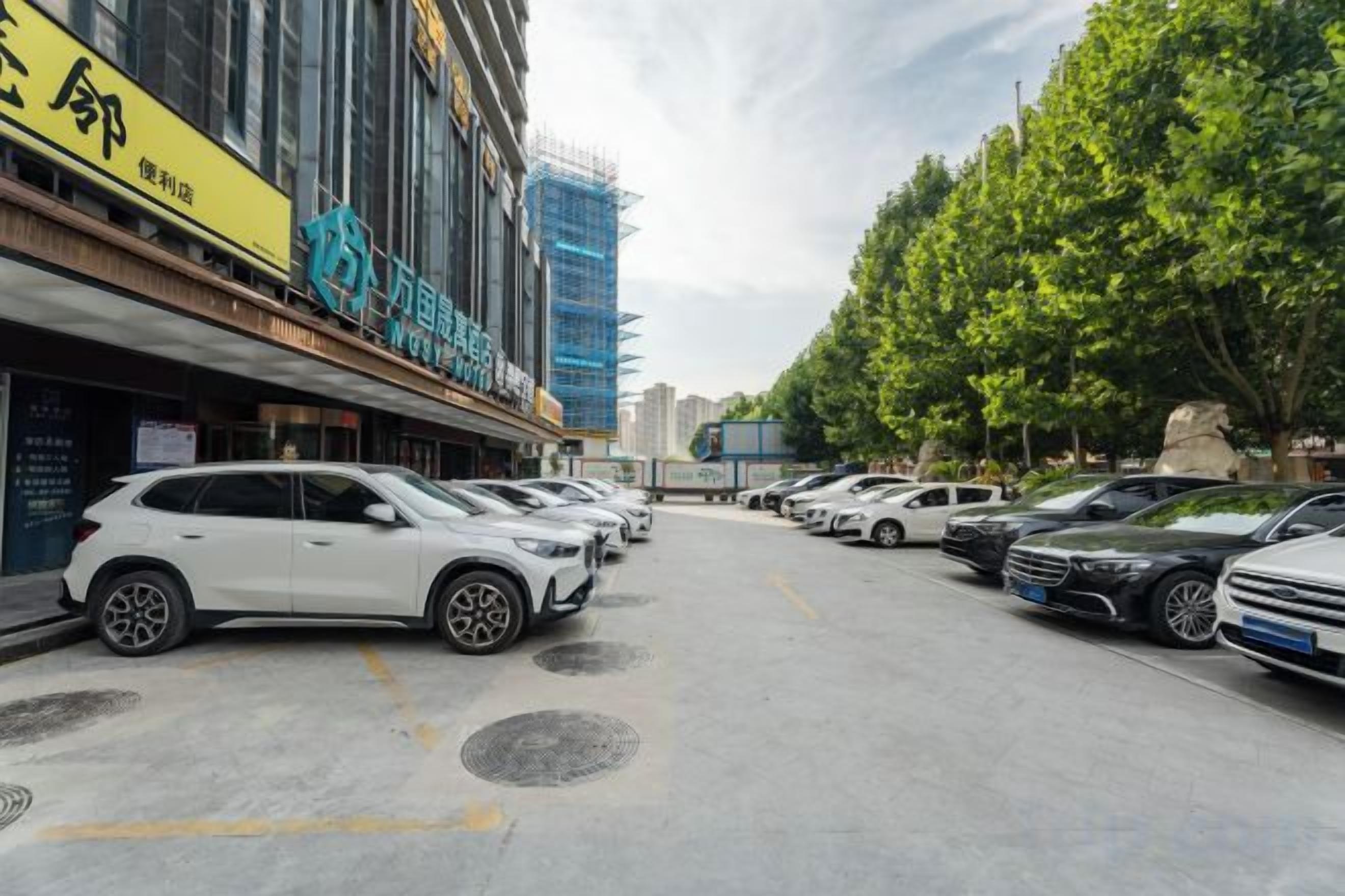 A parking lot with multiple cars, a building with a yellow sign, and trees in the background.