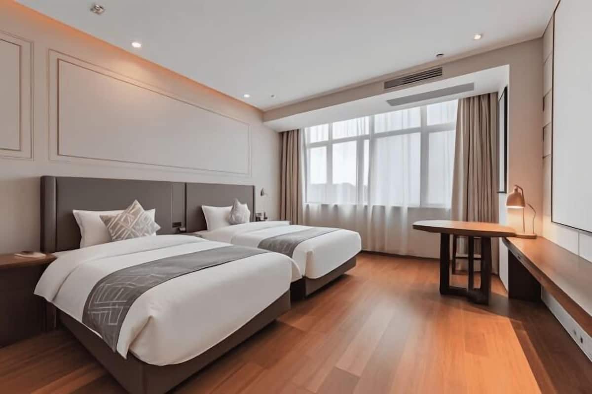 Habitación de hotel con dos camas, piso de madera, una mesita y un ventanal con cortinas.