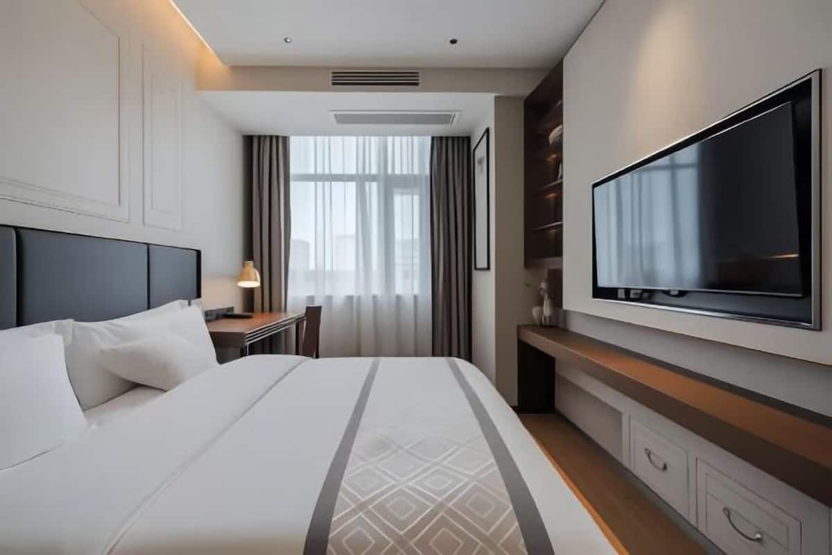 Habitación de hotel con una cama grande, un escritorio, un televisor de pantalla plana montado en la pared y una ventana con cortinas.