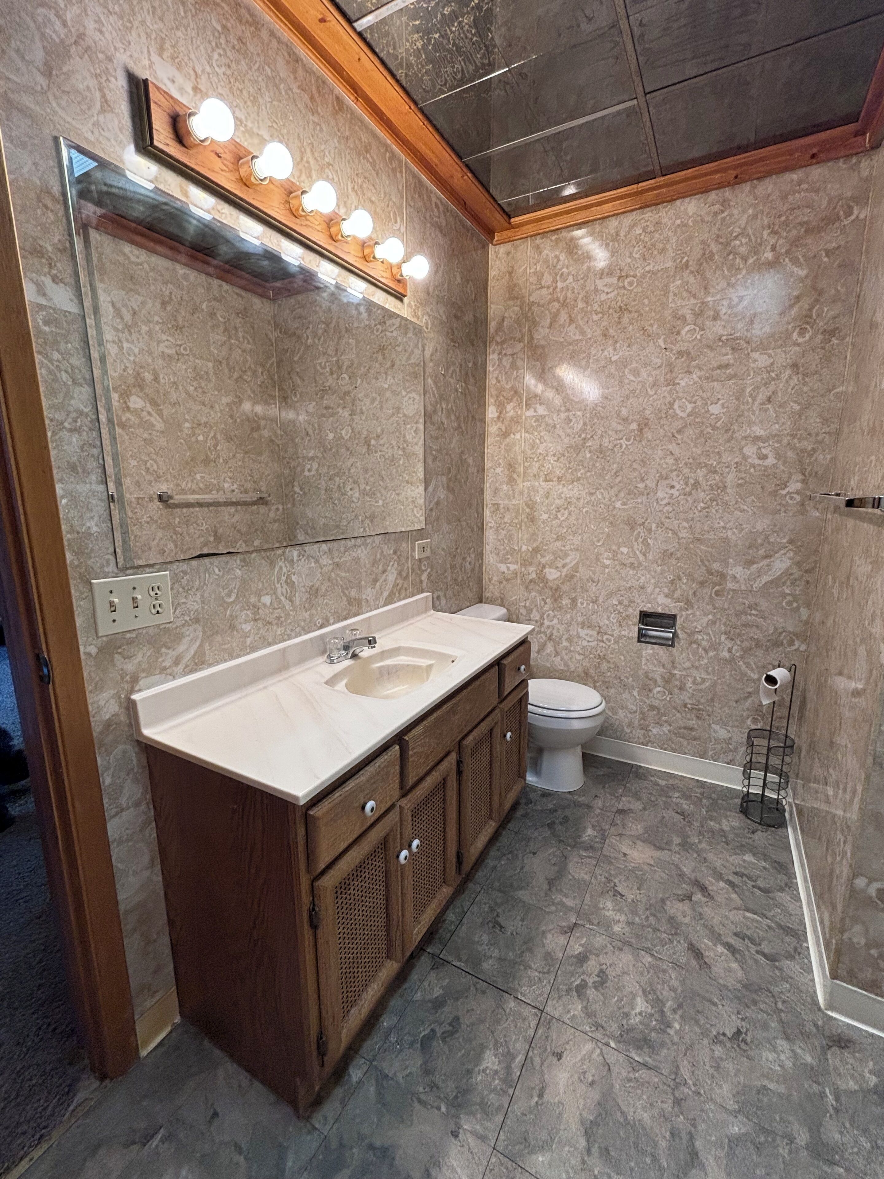 Ein modernes Badezimmer mit Marmorwaschtisch, großem Spiegel mit Beleuchtung, Toilette und Duschbereich.