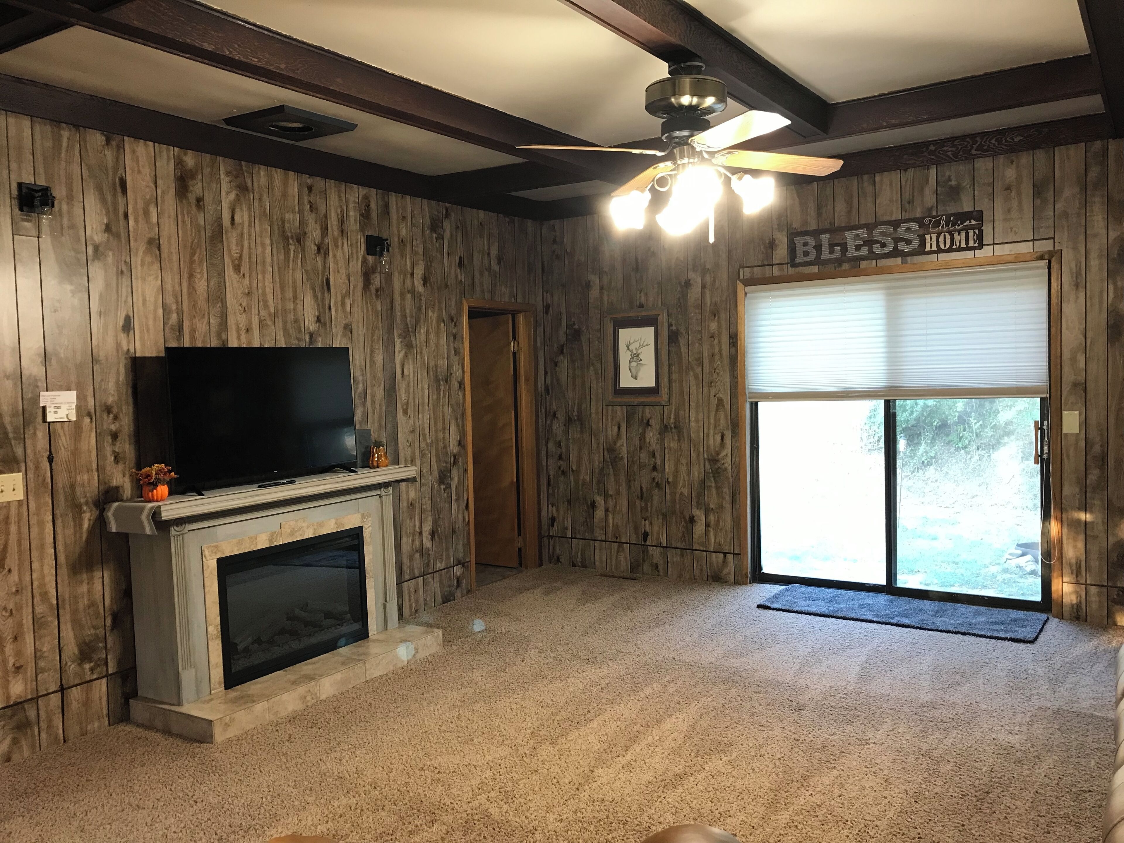 A room with wooden walls, a fireplace, a television, a ceiling fan, and a sliding glass door.