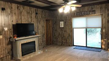 A room with wooden walls, a fireplace, a television, a ceiling fan, and a sliding glass door.