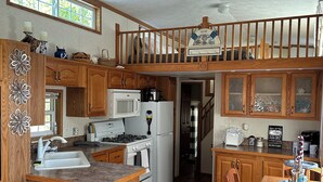 A spacious kitchen with wooden cabinets, a central island, and a dining area with a table and chairs. - 1 bedroom, 2 loft Park Model in campground in Marquette, Iowa.  (Marquette)