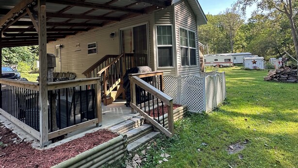 A single-story house with a covered porch, a small deck, and a front yard with grass and mulch. - 1 bedroom, 2 loft Park Model in campground in Marquette, Iowa.  (Marquette)