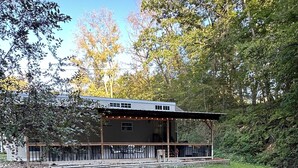 A rustic cabin with a covered porch, surrounded by a grassy yard and dense trees. - 1 bedroom, 2 loft Park Model in campground in Marquette, Iowa.  (Marquette)