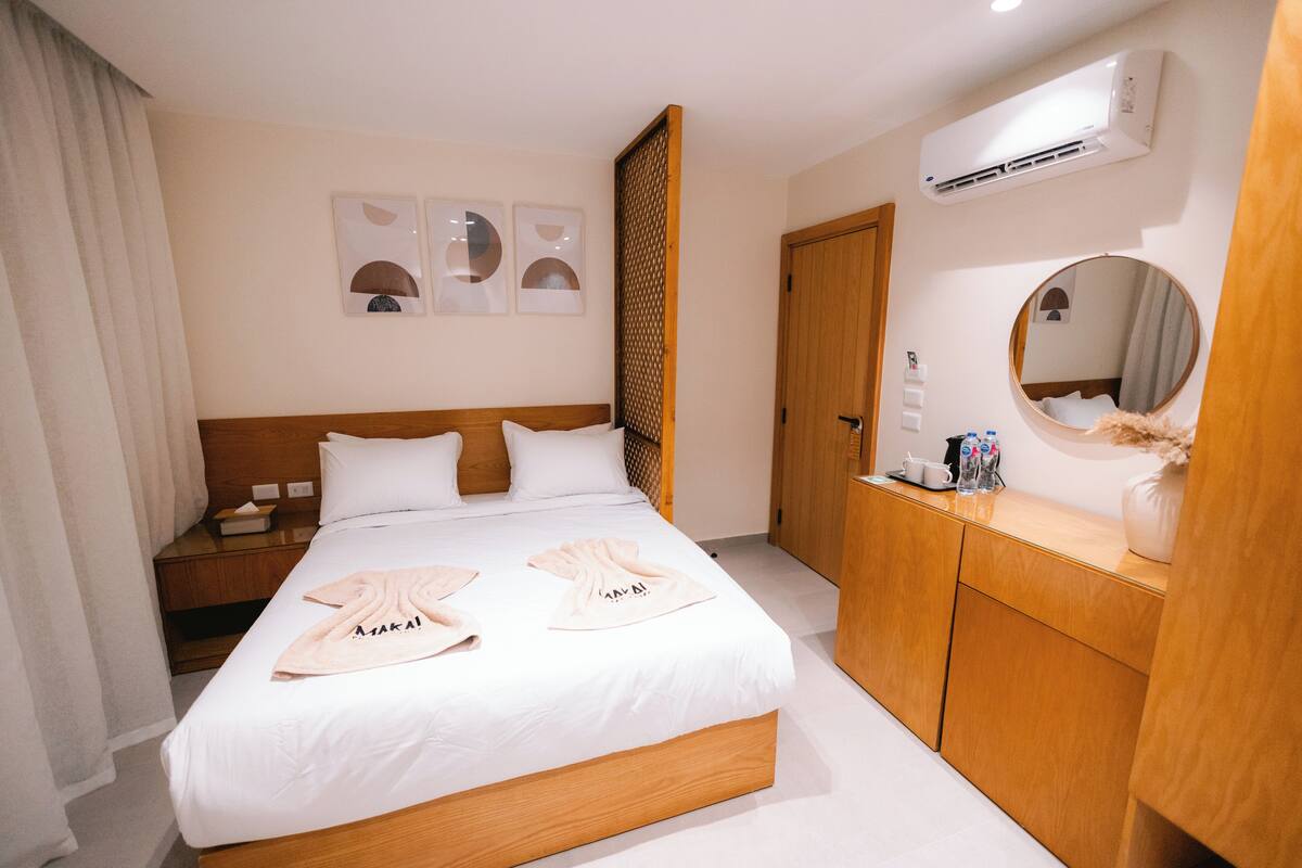 A hotel room with a bed, bedside table, and a mirror.