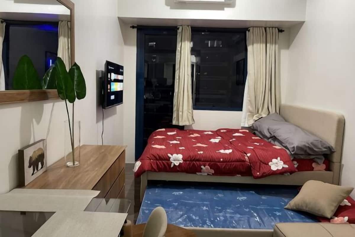 Un dormitorio con cama, escritorio, silla, televisor y ventana con cortinas.