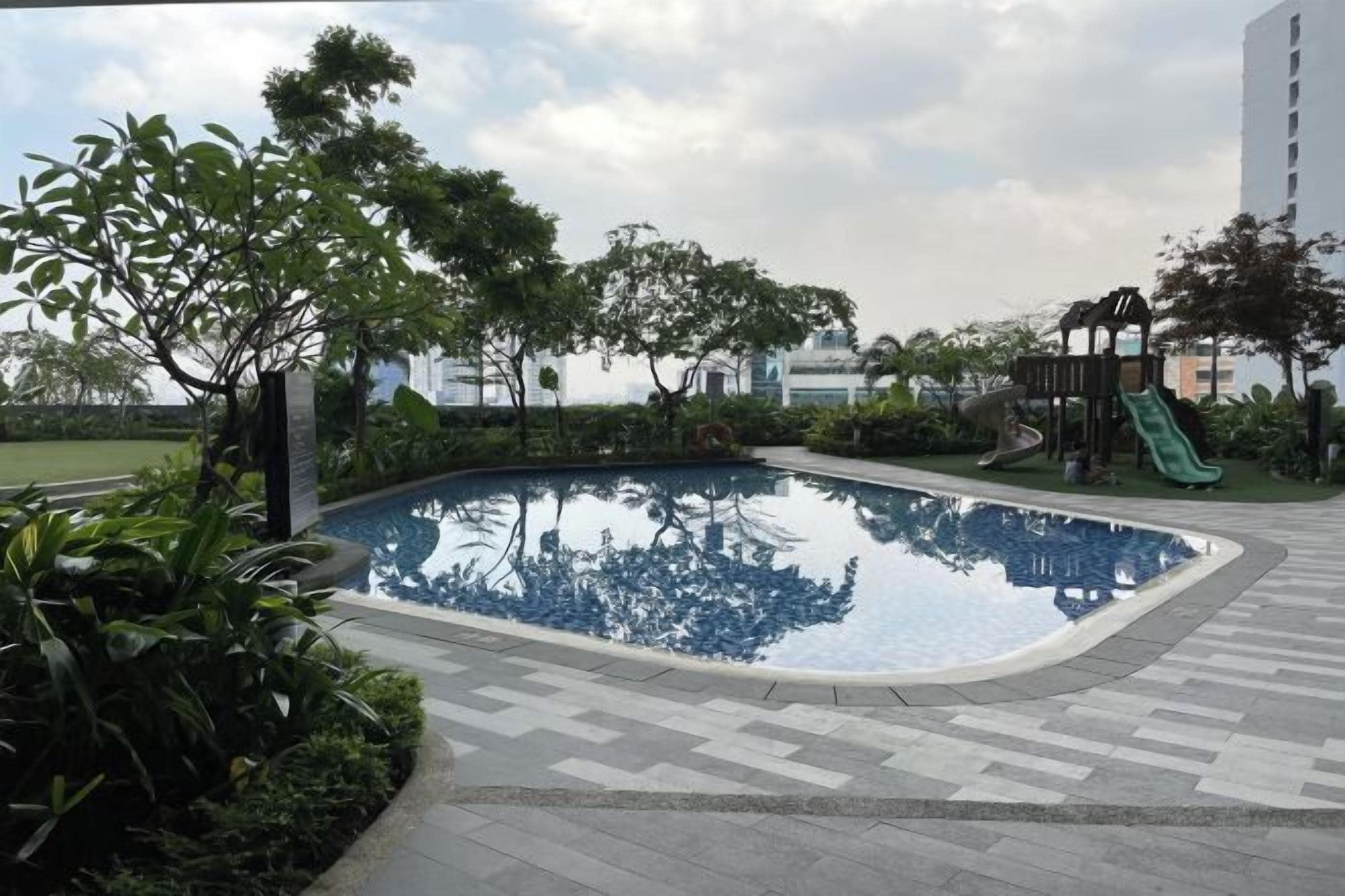 A swimming pool surrounded by greenery and a playground.