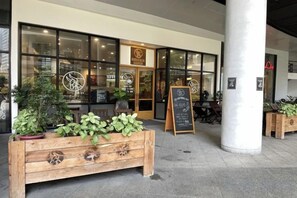 Un restaurante con banco de madera, plantas en macetas y un menú en una pizarra al aire libre.