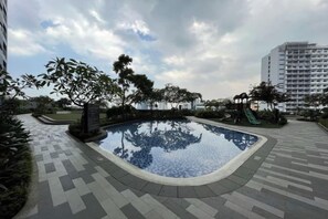 A swimming pool with a paved walkway, surrounded by greenery and a tall building in the background. - Luxury Air Residences By Makati (Makati)