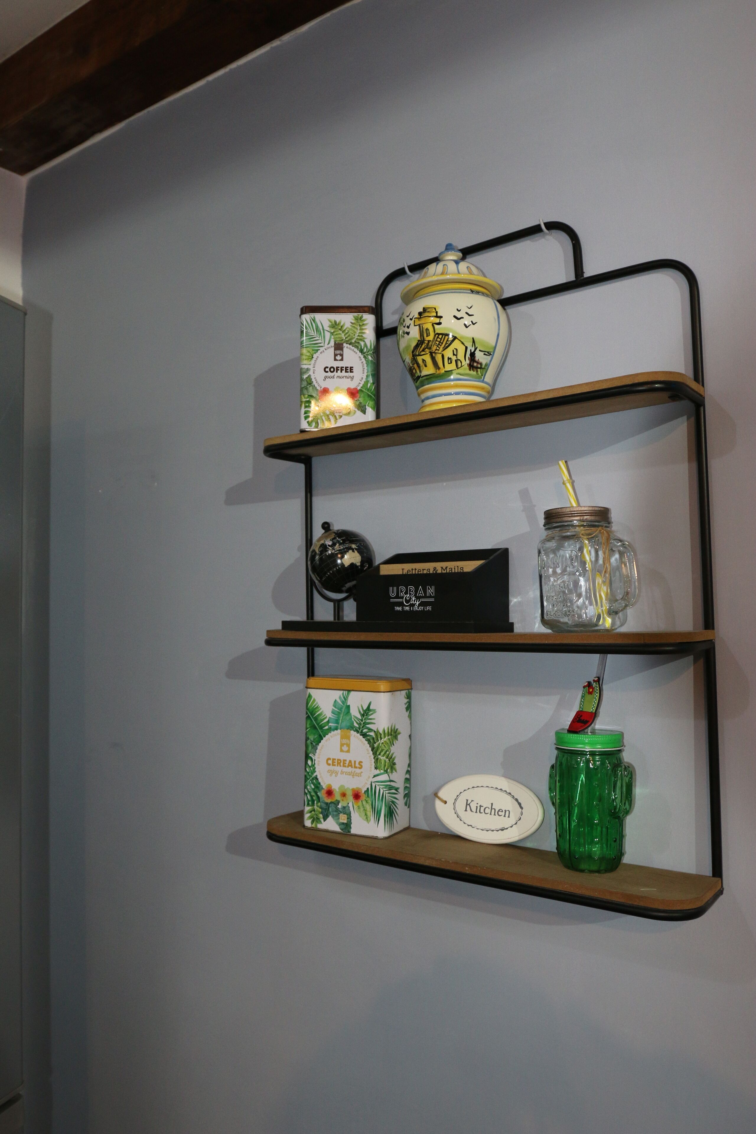 A wall-mounted shelf with various kitchen items including a coffee can, a jar, a box labeled "Letters & Mailla," and a green container.