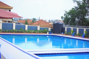 Una piscina con azulejos azules, rodeada por un muro bajo con plantas y algunas sillas azules.