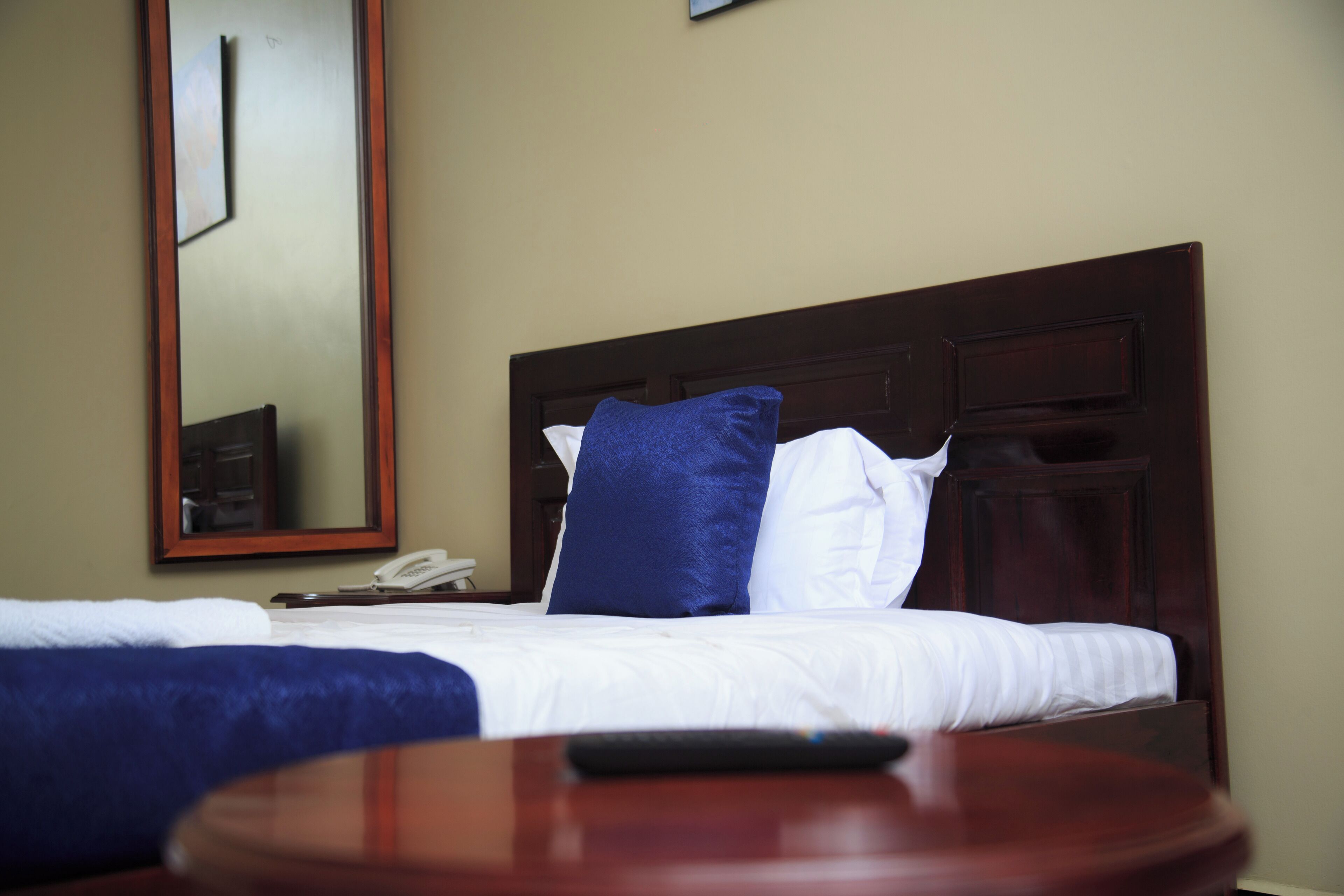 A hotel room with a bed, a bedside table, a mirror, and a telephone.