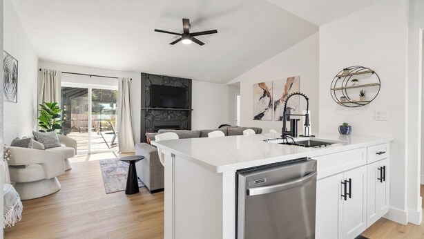 Eine moderne Küche mit weißen Schränken, einem eingebauten Backofen und einem Geschirrspüler. Es gibt einen Essbereich mit einem weißen Tisch und Stühlen sowie ein Wohnzimmer mit einer Couch und einem Couchtisch.