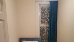 A small, neatly made bed with white bedding and a blue headboard in a room with cream walls and a wooden floor. - Single bedroom near London Seven Kings Train Station (Ilford)