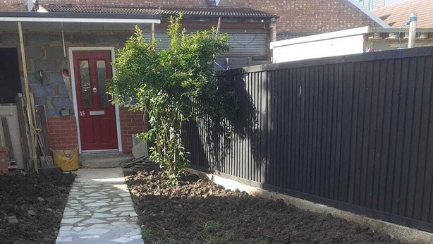 A residential driveway leading to a house with a red door, a garden with a paved path, and a wooden fence. - Single bedroom near London Seven Kings Train Station (Ilford)