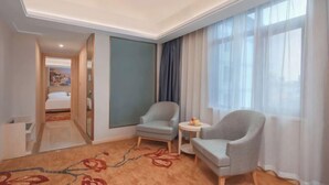 Een hotelkamer met een bed, twee fauteuils, een tafeltje en een groot raam met gordijnen.