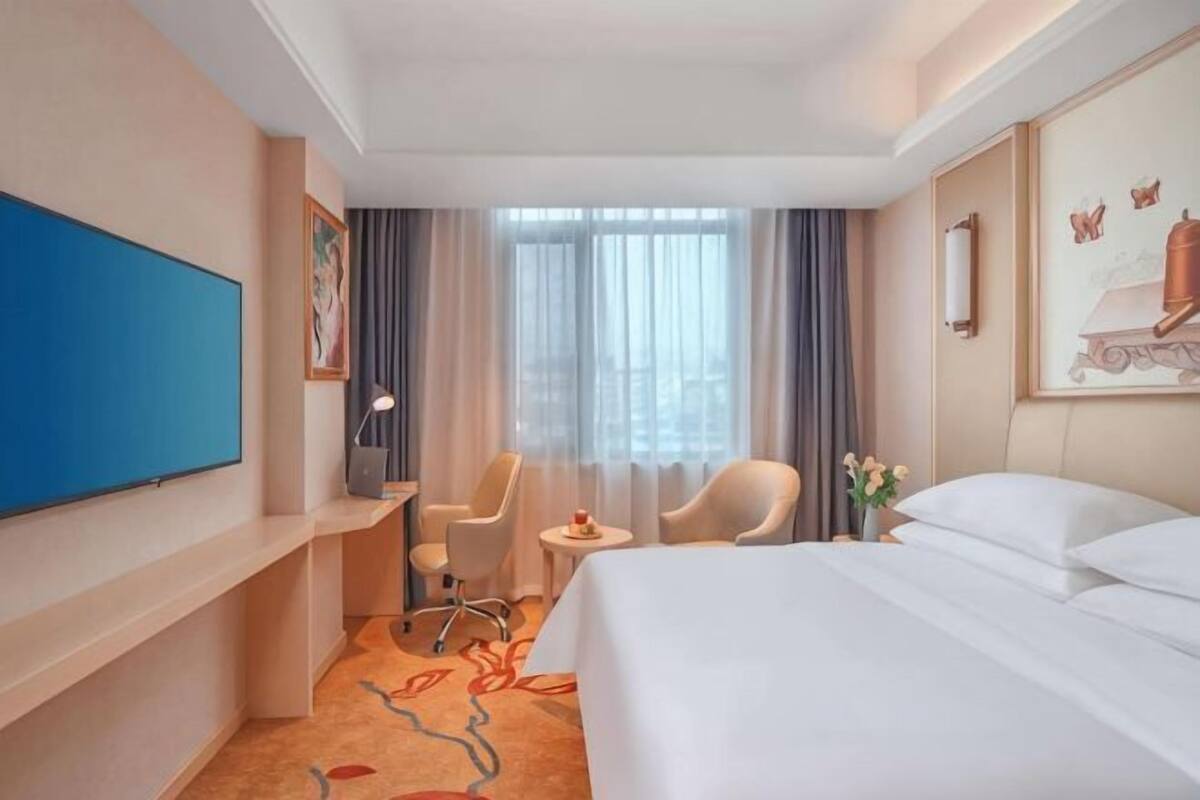 A hotel room with a bed, a desk, a chair, a television, and a window with curtains.