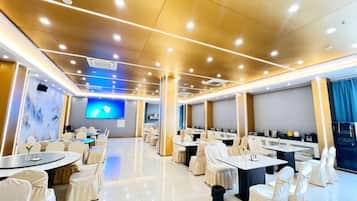 A spacious conference room with round tables and chairs, a large screen, and a modern ceiling design.