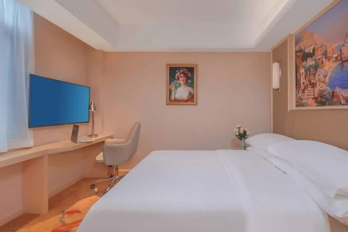 A hotel room with a bed, a desk with a chair, a flat-screen TV, and a painting on the wall.