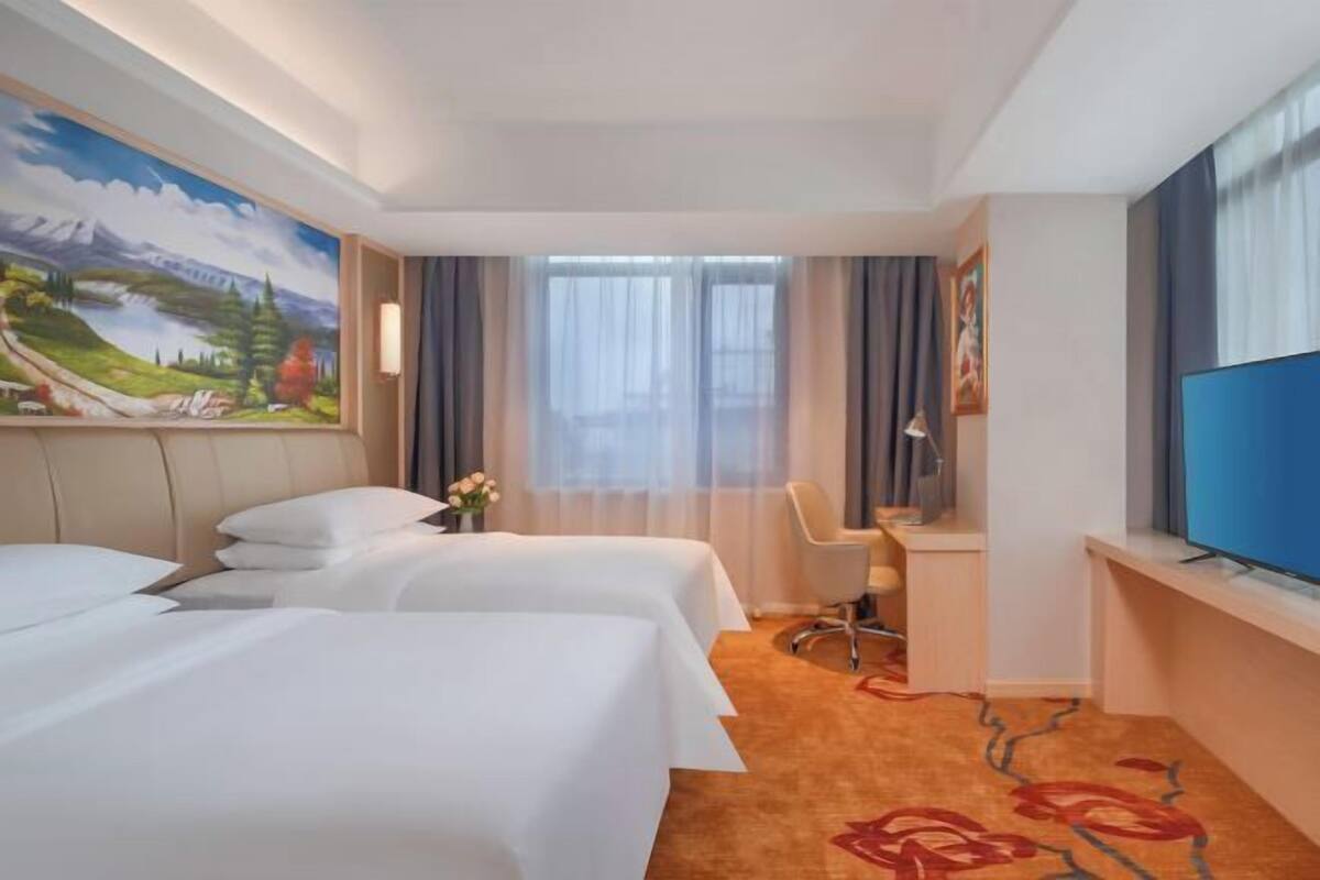 A hotel room with two beds, a desk, a chair, a television, and a painting on the wall.