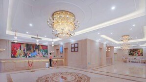 Een ruime lobby met een groot receptiebalie, een kroonluchter en een decoratief vloerpatroon.