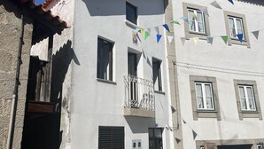 Un bâtiment blanc doté d’un balcon, une voiture garée devant, et des drapeaux aux couleurs vives.