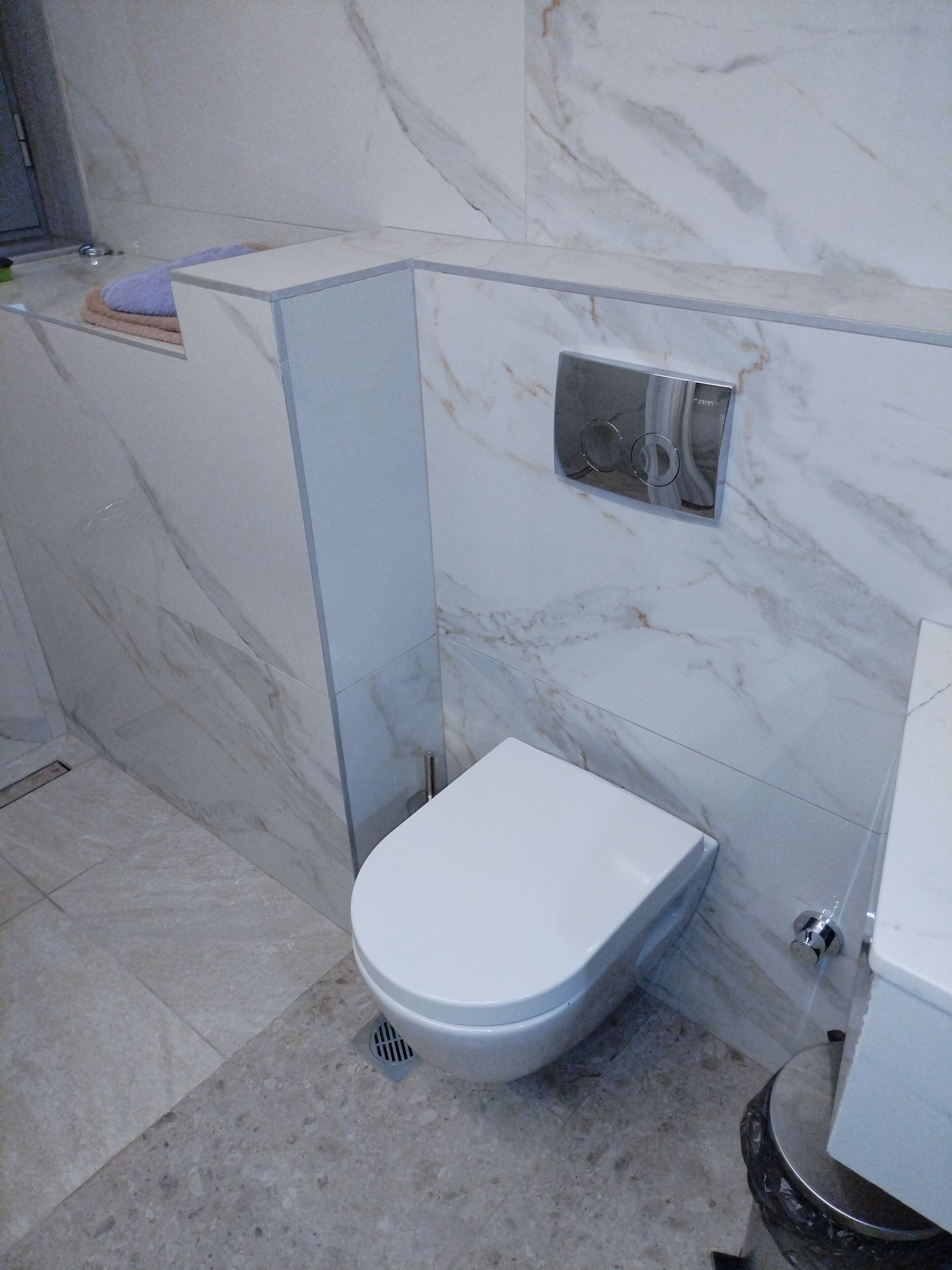 Un baño con inodoro, zona de ducha y pared de mármol.