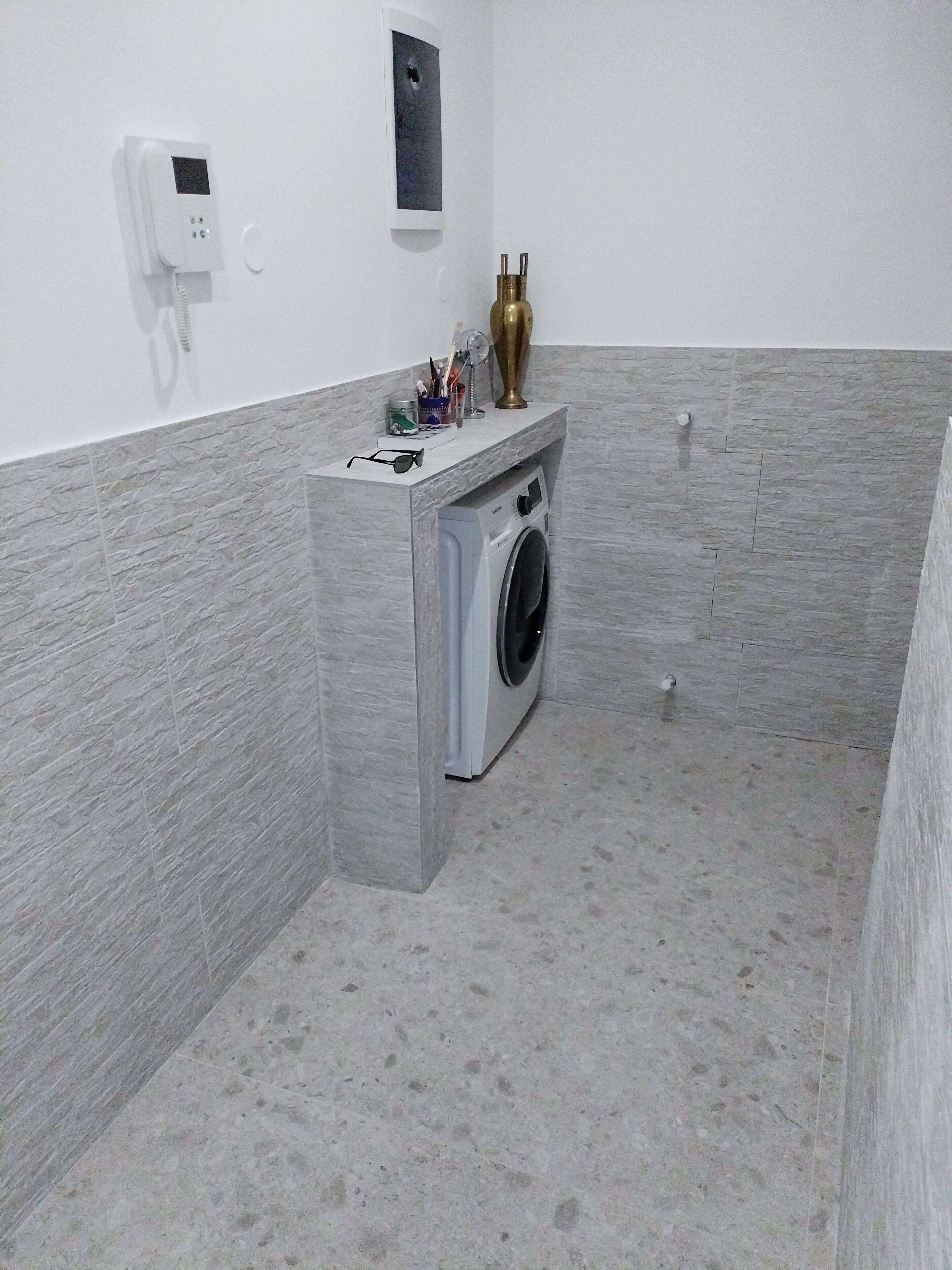 A compact laundry room with a washing machine, a small shelf with toiletries, and a wall-mounted phone.