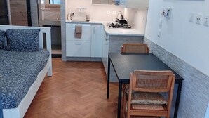 A compact living space with a bed, a dining table with chairs, a kitchenette, and a bathroom.