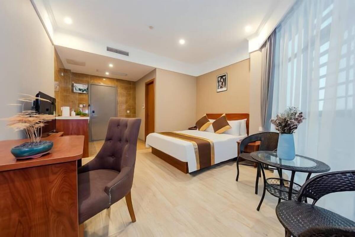 Une chambre d’hôtel avec un lit, un bureau, une chaise, une petite table et une fenêtre avec des rideaux.