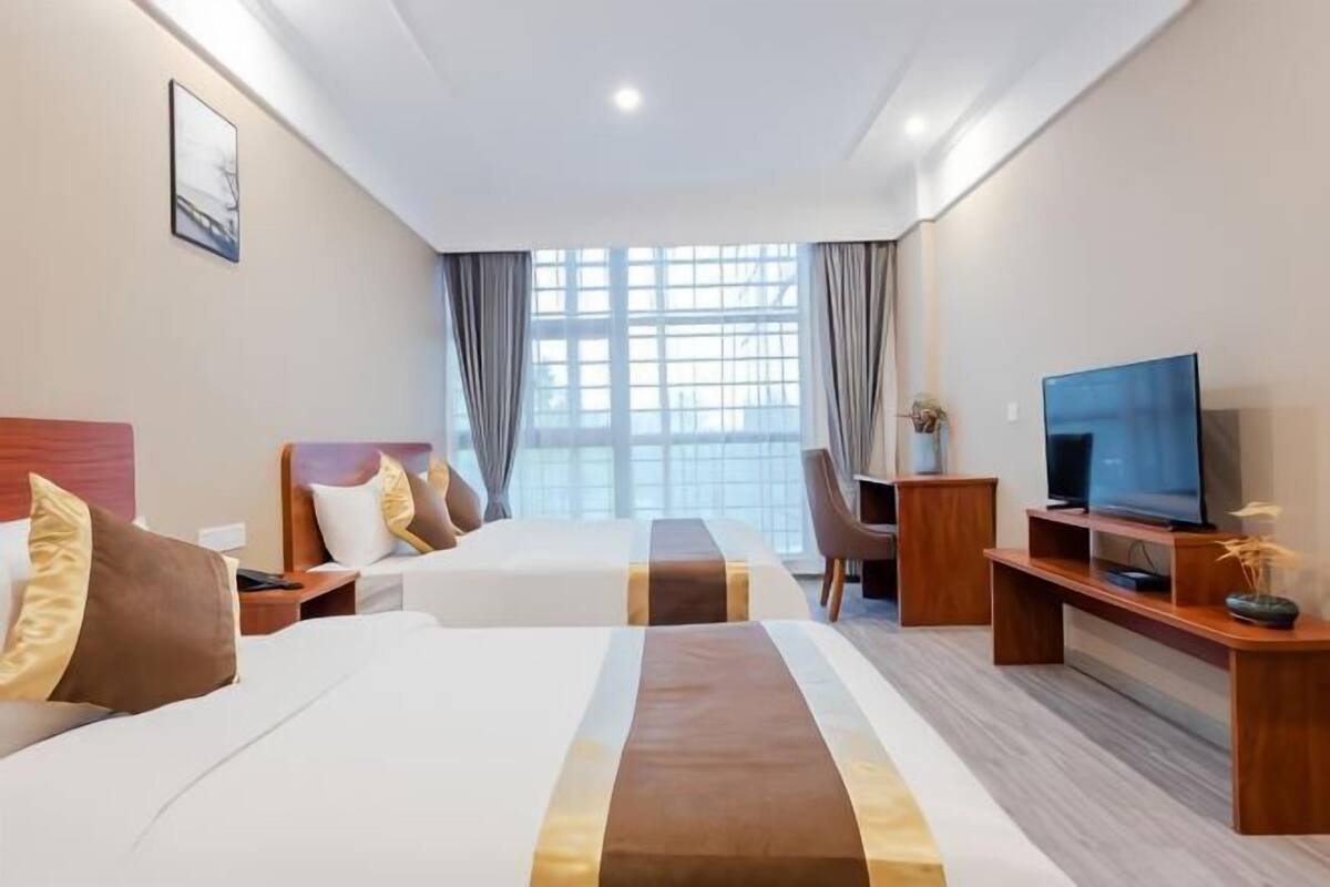 Une chambre d’hôtel avec deux lits, une télévision, un bureau et une grande fenêtre avec des rideaux.