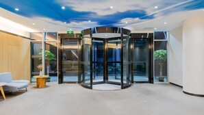 A modern lobby with a revolving door, seating area, and a ceiling with a cloud design.
