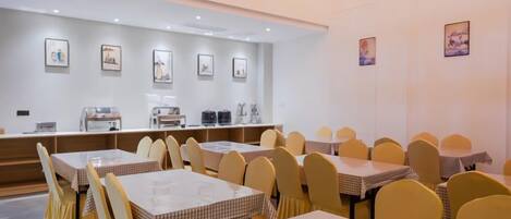 A dining area with multiple tables and chairs, a counter with a coffee machine, and framed pictures on the walls.