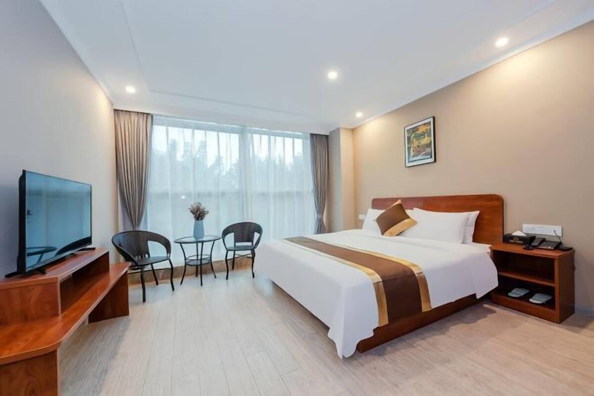 Une chambre d’hôtel comprenant un lit, une table de chevet, une télévision, un bureau, une chaise et une fenêtre avec des rideaux.