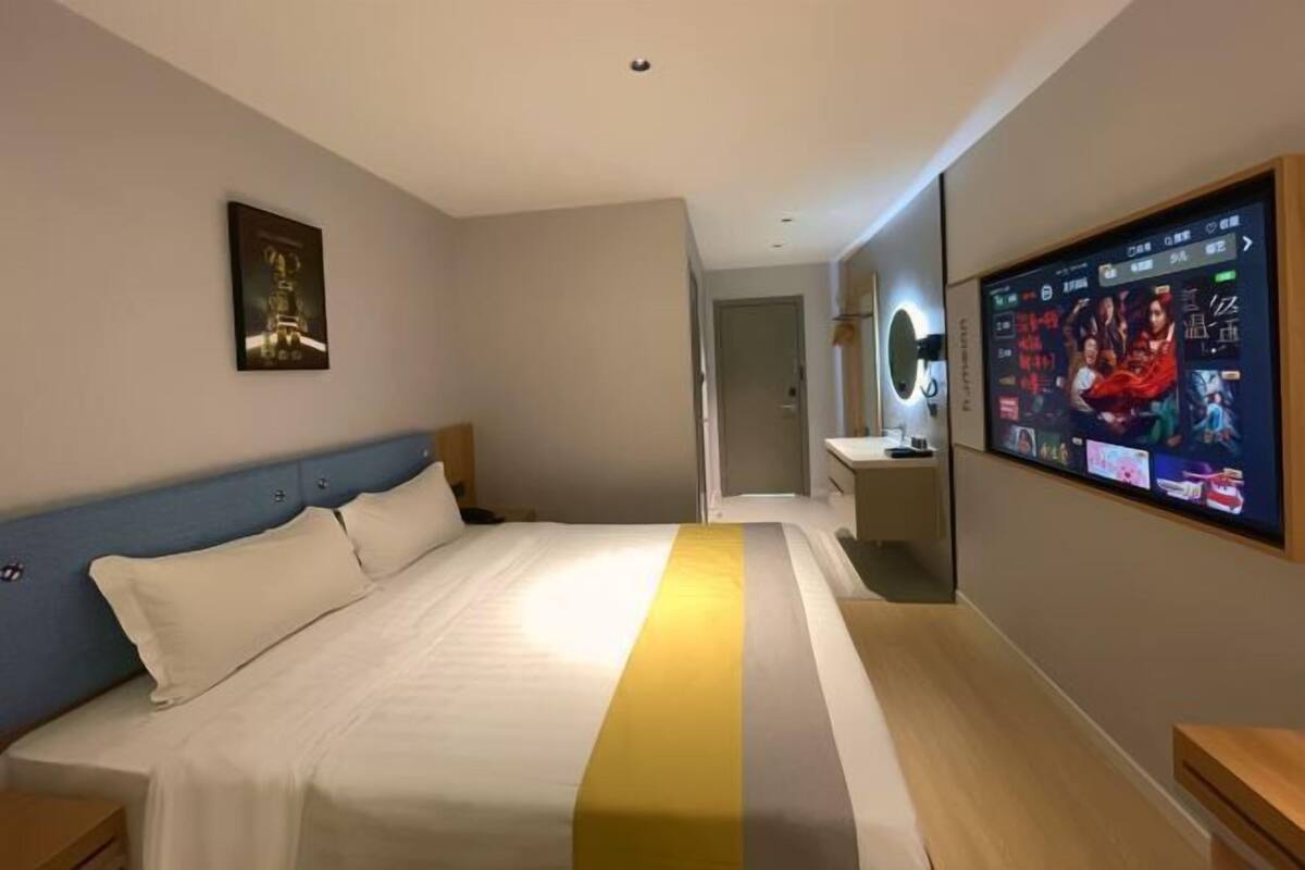 Une chambre d’hôtel avec un lit, un téléviseur fixé au mur, un miroir et un tableau encadré accroché au mur.