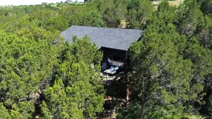 Une cabane entourée d’une forêt dense, dotée d’une petite terrasse et d’un espace extérieur abrité avec des sièges.