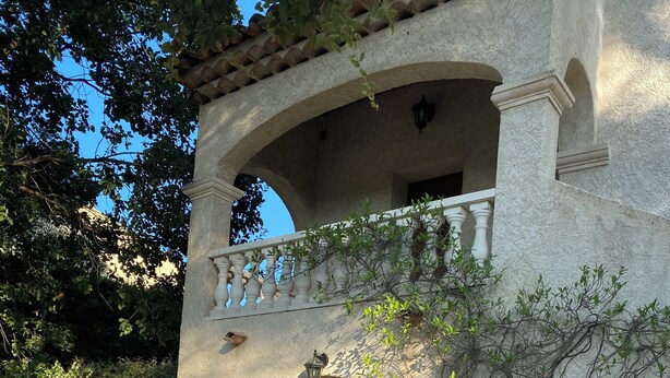 Un patio con mesa y sillas, una pérgola con plantas trepadoras, y un edificio con fachada de piedra y una entrada en arco.