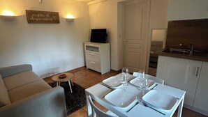 Una sala moderna con comedor, muebles blancos, un televisor de pantalla plana y una cocina con pileta y estufa.