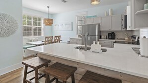 A modern kitchen with a large island, white cabinetry, and a dining area with wooden chairs and a bench. - 30A Driftwood/HotTub/Bikes/Close2Seaside (Santa Rosa Beach)