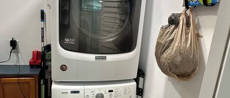 A stacked washer and dryer unit with a shelf above holding laundry detergent and a plastic bag.