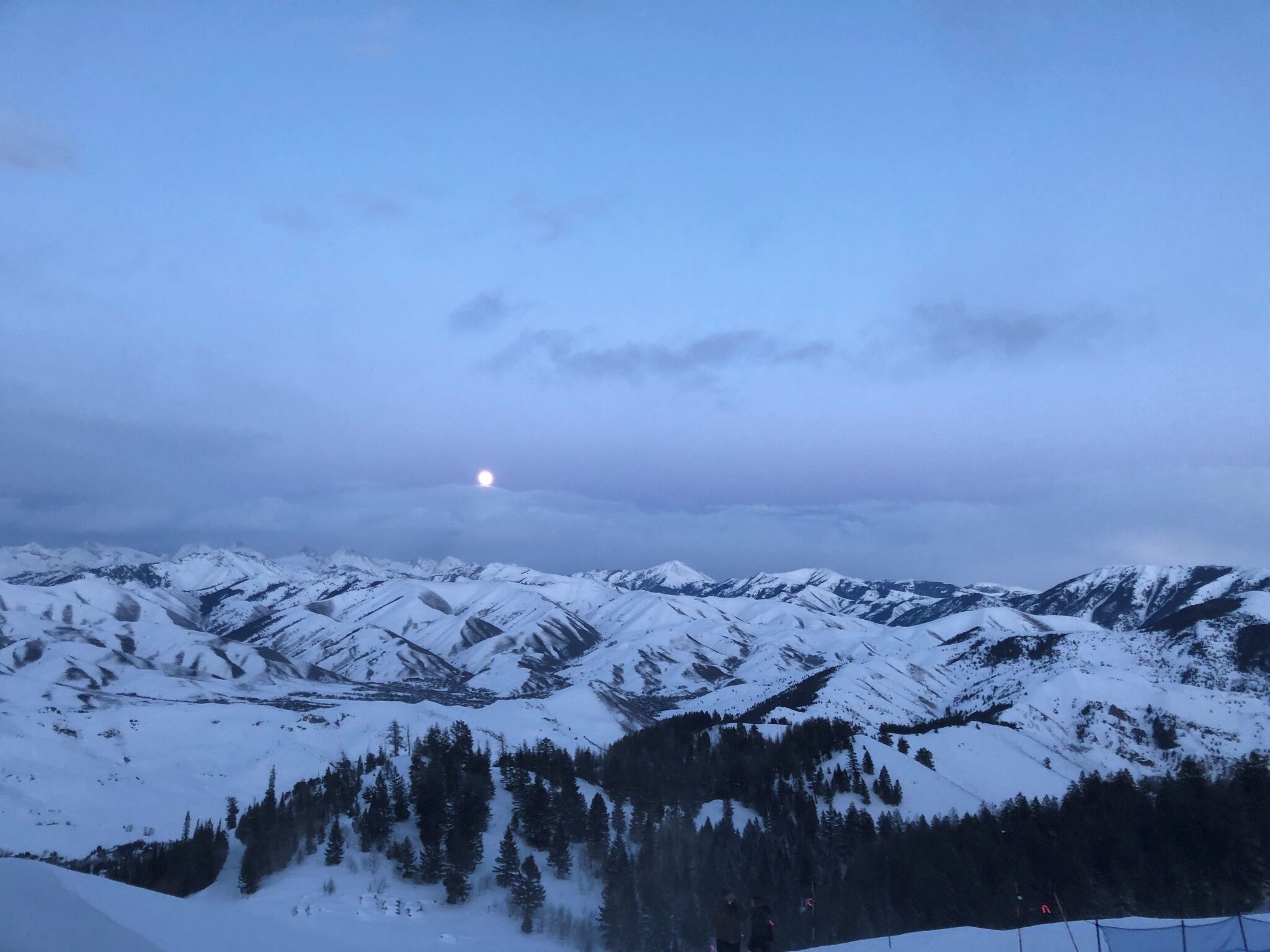 Une chaîne de montagnes enneigée, avec une lune visible dans le ciel.