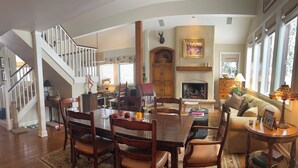 Amplia sala de estar con una gran mesa de comedor de madera, asientos cómodos, una chimenea y una escalera que sube a otro nivel.